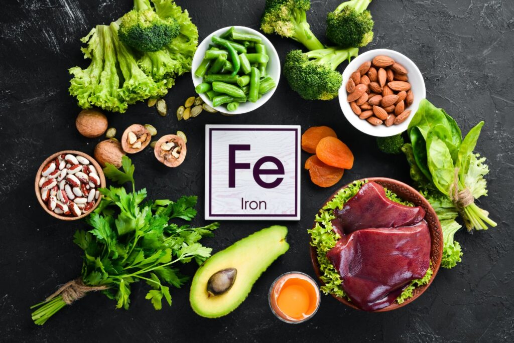 Food containing natural iron. Fe: Liver, avocado, broccoli, spinach, parsley, beans, nuts, on a black stone background. Top view.